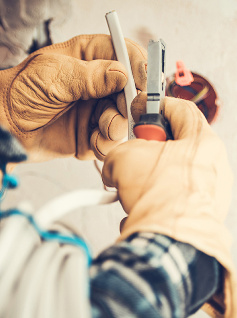 An electrician carrying out work with pliers while wearing thick gloves.