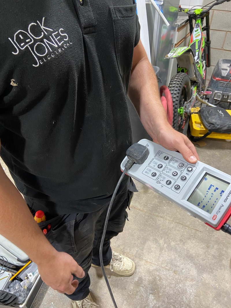 An electrician in a branded Jack Jones shirt holding a PAT testing device